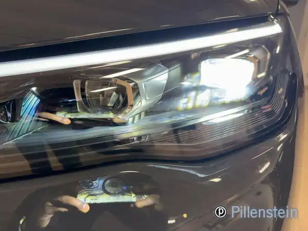 Das Bild zeigt den vorderen linken Scheinwerfer eines schwarzen VW Tiguan in Nahaufnahme. Das Händlerlogo von Pillenstein ist im Bild sichtbar.