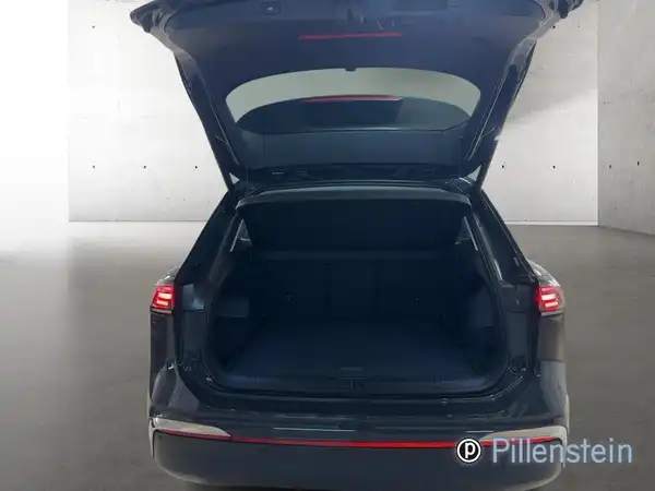 Das Bild zeigt den Kofferraum eines schwarzen VW Tiguan von hinten, mit offenem Kofferraumdeckel. Das Händlerslogo ist sichtbar.