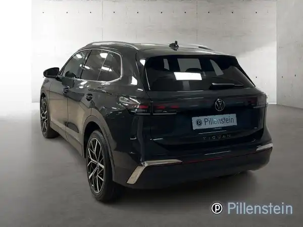 Das Bild zeigt einen schwarzen VW Tiguan von hinten, aufgenommen in einem Verkaufsraum. Es ist das Händlerlogo von Pillenstein auf dem Bild sichtbar.