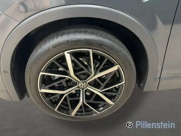 Das Bild zeigt die Felge eines grauen VW Tiguan, aufgenommen von der Seite, mit einem Händlerlogo.