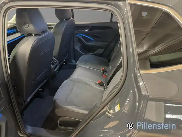 Das Bild zeigt den Innenraum eines VW Tiguan von hinten, mit schwarzen Sitzen und grauem Exterieur. Es ist ein Händlerlogo eingeprägt.