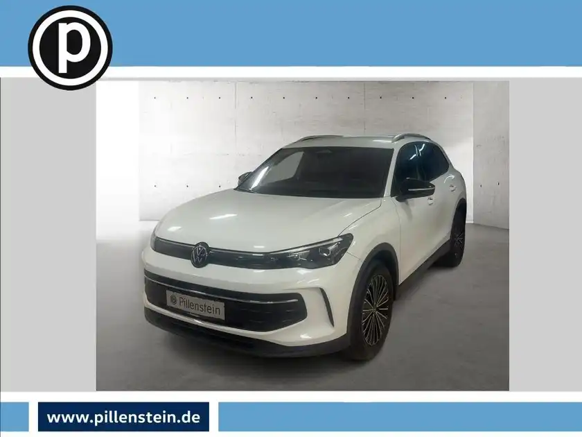 Das Bild zeigt einen weißen VW Tiguan, aufgenommen von vorne. Es enthält das Händlerlogo oben links und auch andere markante Texteinblendungen.