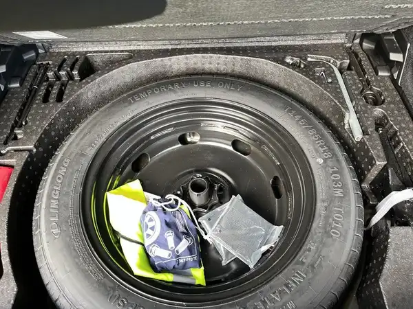 Das Bild zeigt den Kofferraum eines Fahrzeugs, in dem ein Ersatzreifen und weiteres Zubehör zu sehen sind. Es handelt sich um eine Innenaufnahme des Fahrzeugs.