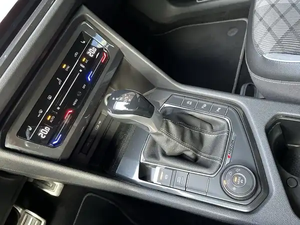 Eine Innenaufnahme des Fahrzeugs zeigt das Armaturenbrett und die Schaltkonsole des VW Tiguan in schwarzer Kunststoffausführung.