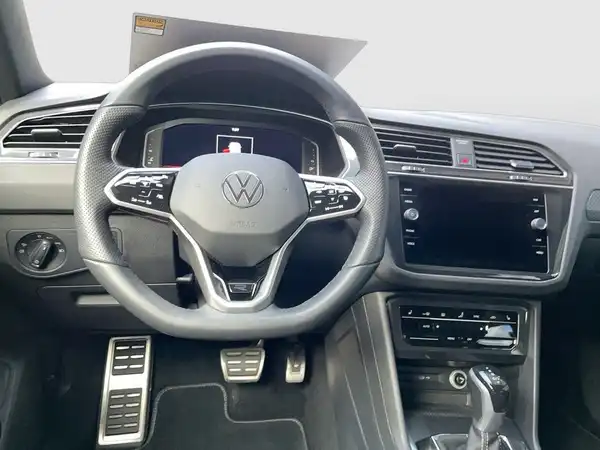 Das Bild zeigt das Innere eines VW Tiguan mit einem sportlichen schwarzen Interieur. Die Aufnahme ist vom Fahrersitz aus aufgenommen, wobei das Lenkrad und das Infotainmentsystem sichtbar sind.