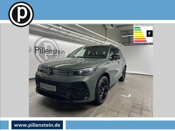 Das Bild zeigt einen grauen VW Tiguan von der Seite in einer Ausstellungshalle, mit dem Händlerlogo von Pillenstein im Hintergrund.