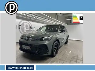 Das Bild zeigt einen grauen VW Tiguan von der Seite in einer Ausstellungshalle, mit dem Händlerlogo von Pillenstein im Hintergrund.