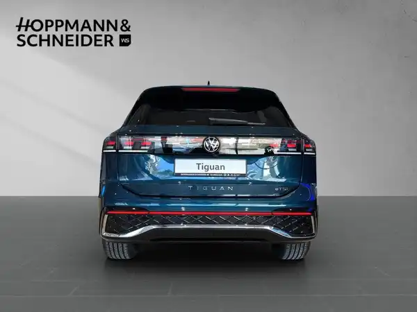 Das Bild zeigt die Rückansicht eines blauen VW Tiguan. Im oberen Bereich des Bildes ist das Händlerlogo "HOPPMANN & SCHNEIDER" eingeblendet.
