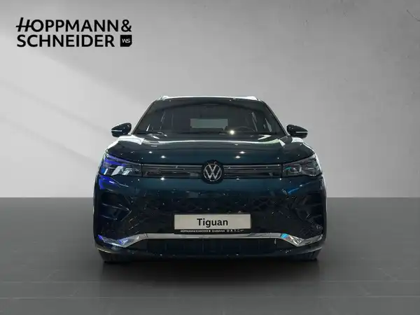 Das Bild zeigt einen Volkswagen Tiguan von vorne, in einer grünen Farbe. Oben links ist das Händlerlogo 'HOPPMANN & SCHNEIDER' sichtbar, und es enthält markante Texteinblendungen.