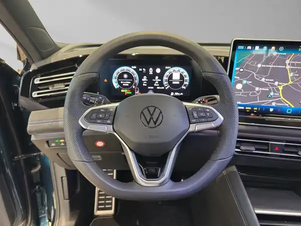 Das Bild zeigt das Interieur eines VW Tiguan mit einem schwarzen Innenraum und einem modernen Cockpit, einschließlich eines digitalen Anzeigenfelds und eines Navigationssystems.