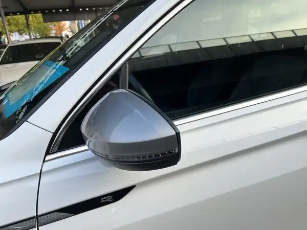 Das Bild zeigt die seitliche Ansicht eines weißen VW Tiguan Allspace, insbesondere den Seitenspiegel und die Fenster.