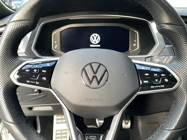 Das Bild zeigt das Innenraum eines Volkswagen Tiguan, insbesondere das Lenkrad und das Cockpit-Display. Die Innenfarbe ist schwarz.
