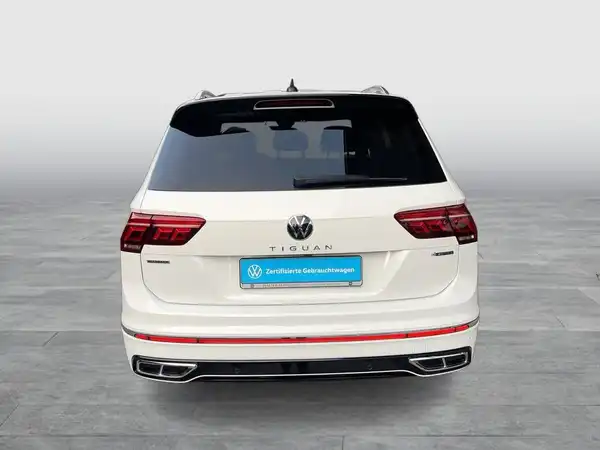 Eine Aufnahme von hinten des weißen VW Tiguan Allspace mit einem Händlerlogo und markanten Texteinblendungen.