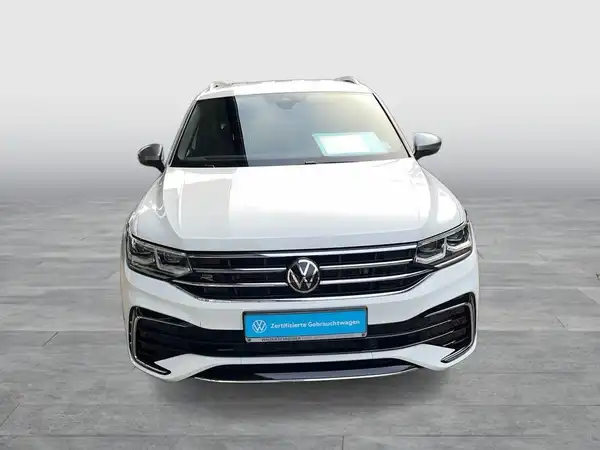 Das Bild zeigt einen weißen VW Tiguan Allspace von vorne, es gibt ein Händlertestimonial im Bild.