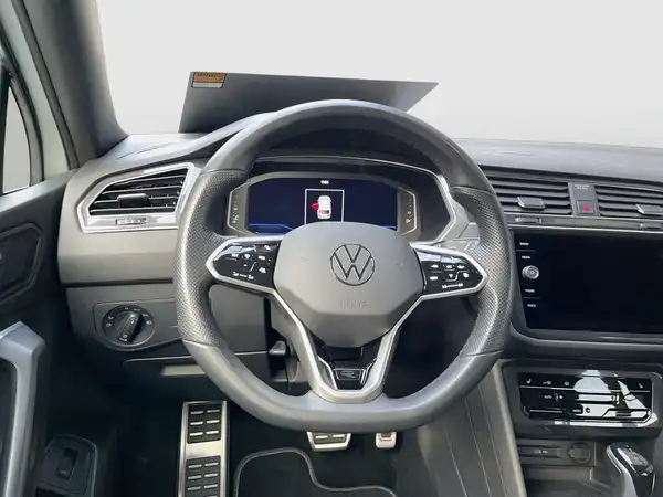 Das Bild zeigt das Innere eines VW Tiguan Allspace, aufgenommen aus dem Blickwinkel des Fahrers. Das Interieur ist in Schwarz gehalten, ohne sichtbare Händlerlogos oder markante Texteinblendungen.