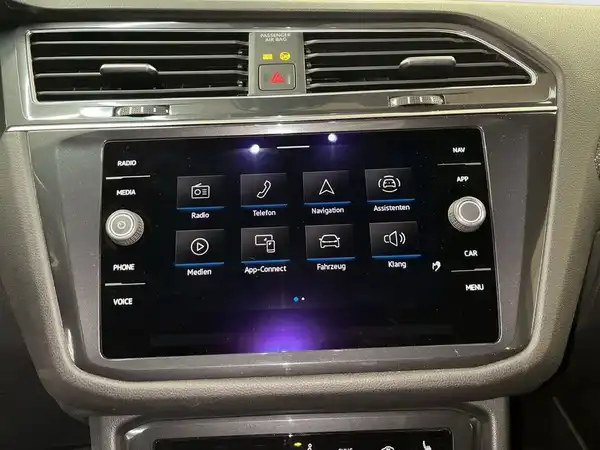 Das Bild zeigt den Innenraum eines VW Tiguan Allspace mit einem modernen Infotainmentsystem. Der Bildschirm enthält verschiedene Menüoptionen wie Radio, Telefon und Navigation.