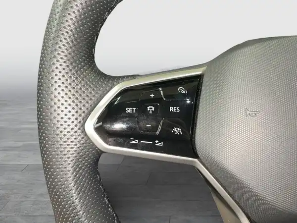 Das Bild zeigt das Lenkrad des VW Tiguan Allspace aus dem Innenraum, es ist schwarz und hat verschiedene Bedienelemente.