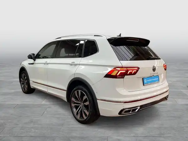 Das Bild zeigt einen weißen VW Tiguan Allspace von hinten aufgenommen, mit sichtbaren Texteinblendungen.
