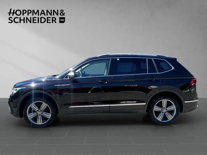 Das Bild zeigt einen seitlichen Blick auf einen schwarzen VW Tiguan Allspace. Im Hintergrund ist das Händlerlogo 'HOPPMANN & SCHNEIDER' sichtbar.