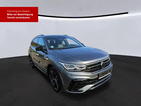 Das Bild zeigt einen grauen VW Tiguan Allspace aus der Seitenansicht. Oben links ist eine markante Texteinblendung in roter Schrift sichtbar, die darauf hinweist, dass das Fahrzeug im Vorlauf ist und Termine zur Besichtigung vereinbart werden können.