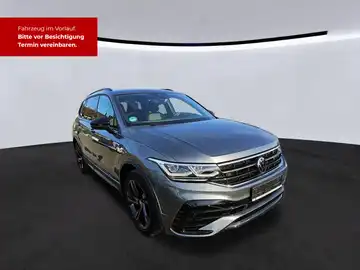 Das Bild zeigt einen grauen VW Tiguan Allspace aus der Seitenansicht. Oben links ist eine markante Texteinblendung in roter Schrift sichtbar, die darauf hinweist, dass das Fahrzeug im Vorlauf ist und Termine zur Besichtigung vereinbart werden können.