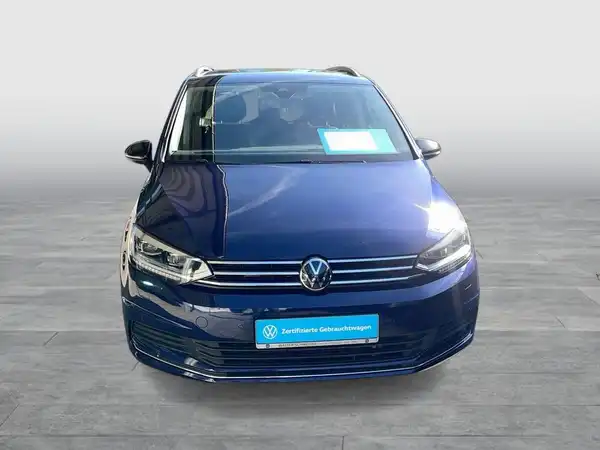 Das Bild zeigt einen blauen VW Touran von vorne. Es enthält eine markante Texteinblendung.