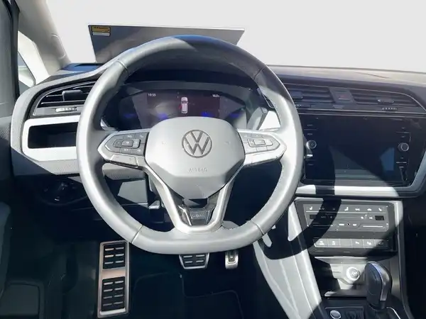 Das Bild zeigt das Interieur eines VW Touran mit einem schwarzen Cockpit und Lenkrad.