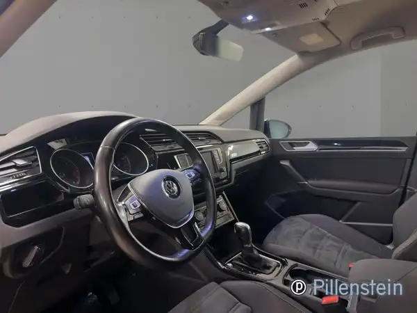 Das Bild zeigt das Innere eines VW Touran mit schwarzem Interieur sowie dem Händlerlogo von Püllenstein.