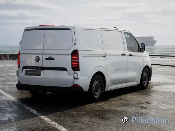 Das Bild zeigt einen weißen VW Transporter Kasten von hinten auf einem Parkplatz mit Meerblick.
