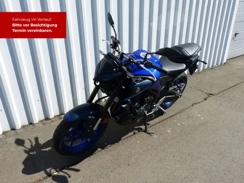 Das Bild zeigt eine YAMAHA MT-03 von der Seite in blau. Es enthält textliche Informationen über die Fahrzeugbesichtigung.