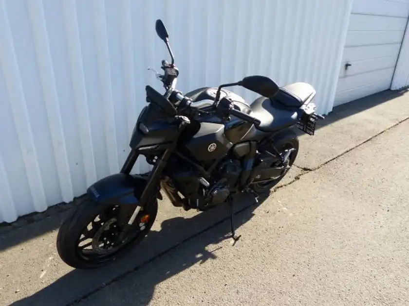 Das Bild zeigt eine schwarze Yamaha MT-07 von der Seite, geparkt auf einer asphaltierten Fläche.