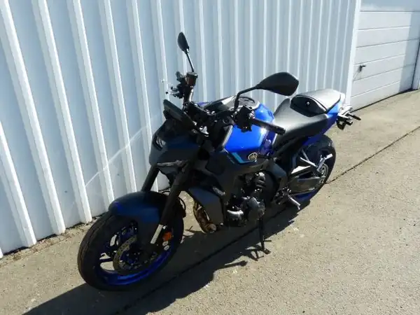 Das Bild zeigt ein Fahrzeug, eine Yamaha MT-09, von der Seite in blauer Farbe. Die Aufnahme scheint im Freien an einer Wand gemacht worden zu sein.