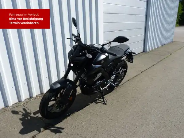 Das Bild zeigt eine schwarze Yamaha MT-125 von der Seite. Im Hintergrund ist ein Gebäude zu sehen. Es gibt eine markante Texteinblendung in Rot mit dem Hinweis, dass das Fahrzeug im Vorlauf ist und eine Besichtigungstermin vereinbart werden sollte.