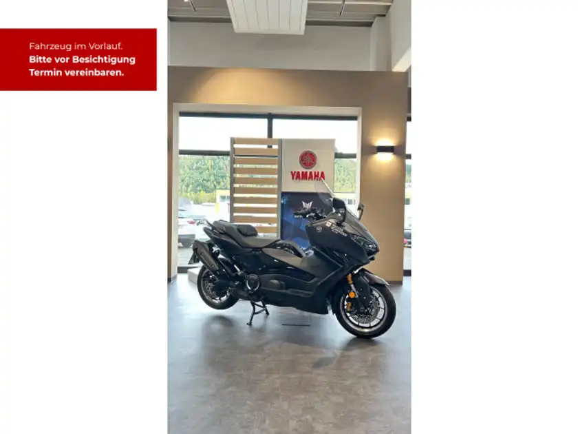 Das Bild zeigt einen schwarzen YAMAHA TMAX von der Seite in einem Verkaufsraum, mit einem Händlerlogo und weiteren Texteinblendungen, die auf einen Besichtigungstermin hinweisen.