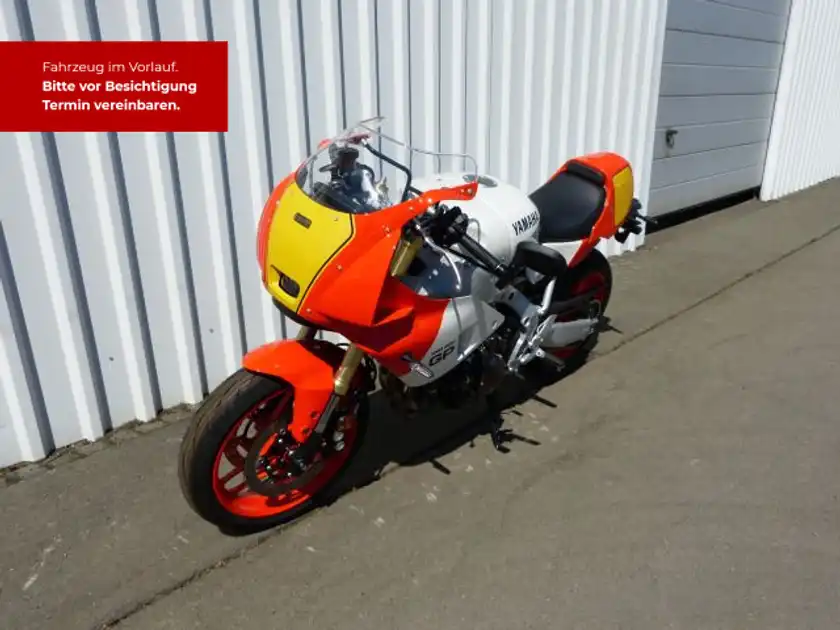 Das Bild zeigt eine YAMAHA XSR 900 von der Seite in orange und weiß, mit markanten Texteinblendungen.